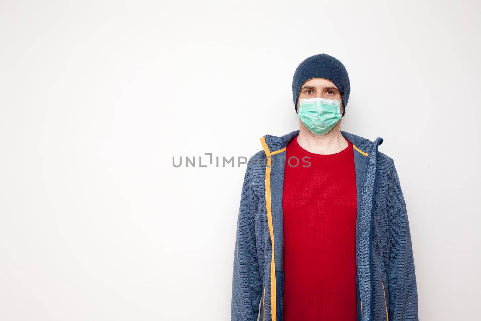 Man with green protective mask on white background. A man with a red sweater and a blue jacket, with a hood.