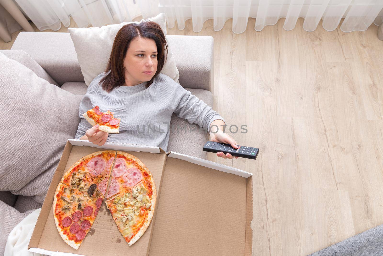 Woman laying on couch with cell phone eating pizza