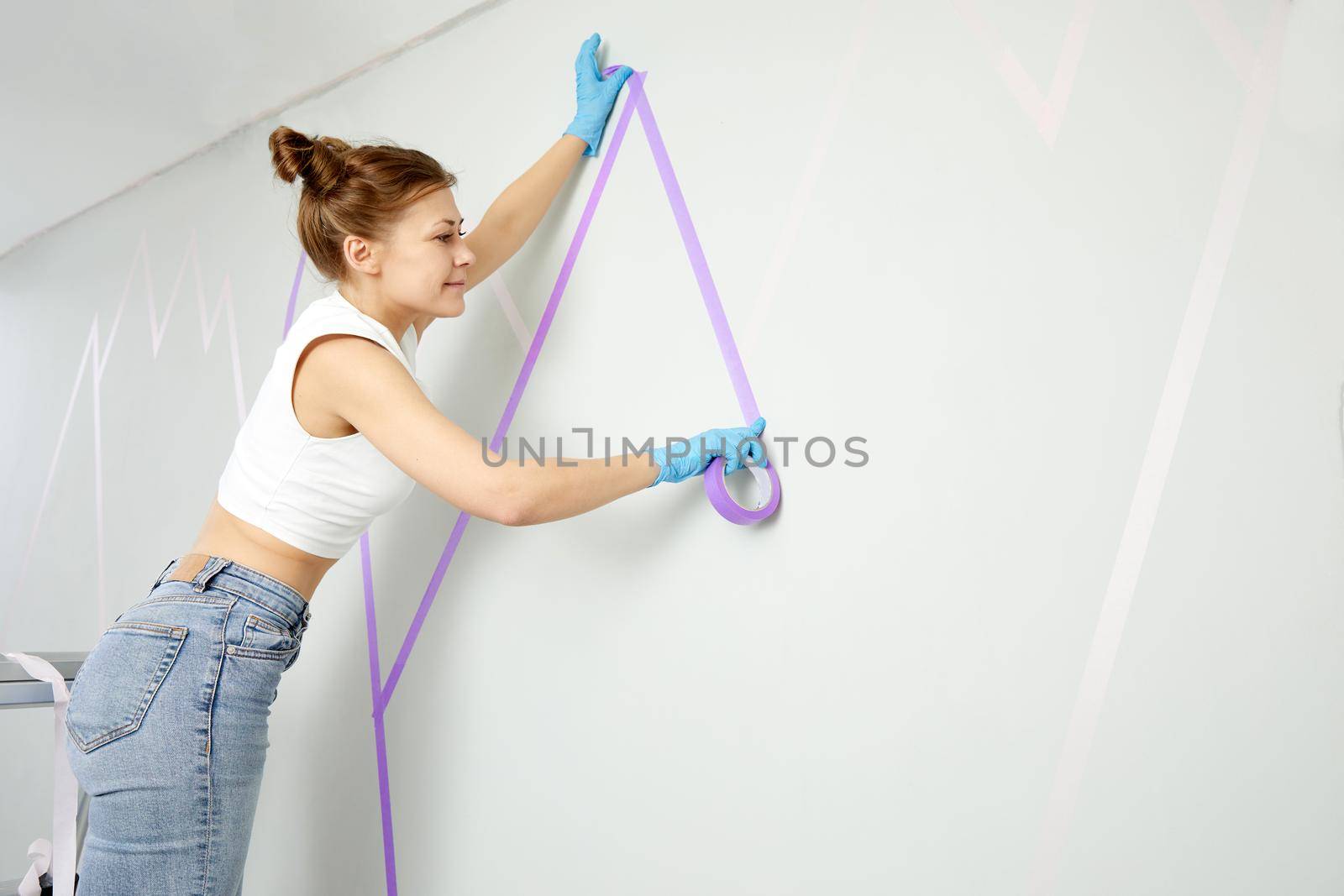 Young woman preparing wall for painting standing on ladder. Diy project with copy space