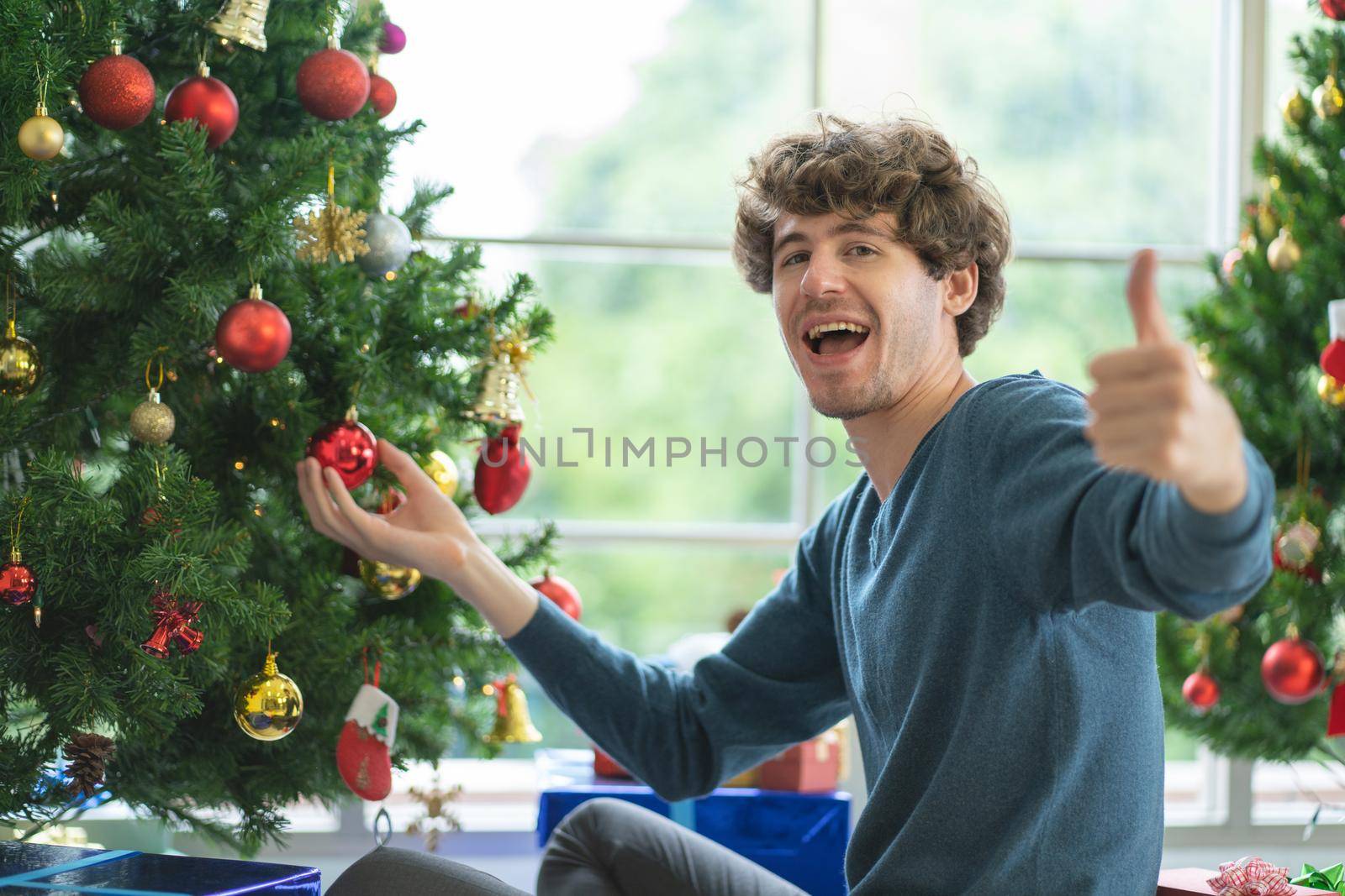 Caucasian man show thumbs up to camera during decorate the Christmas tree with happiness to stay at home and celebrating.