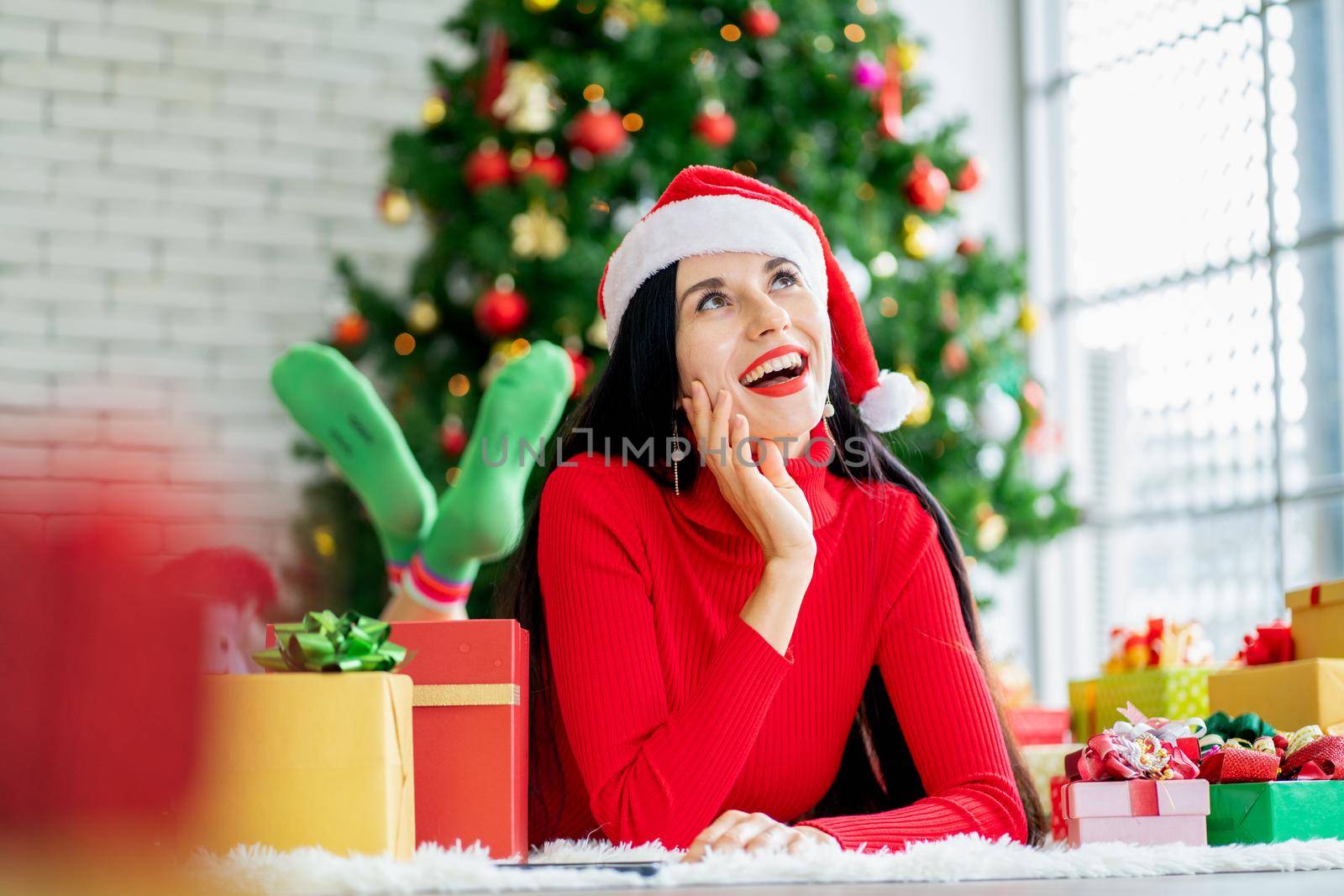 Pretty woman with Christmas costume lie on floor and look up on right side with smiling like exciting with the present and Christmas tree as background. by nrradmin