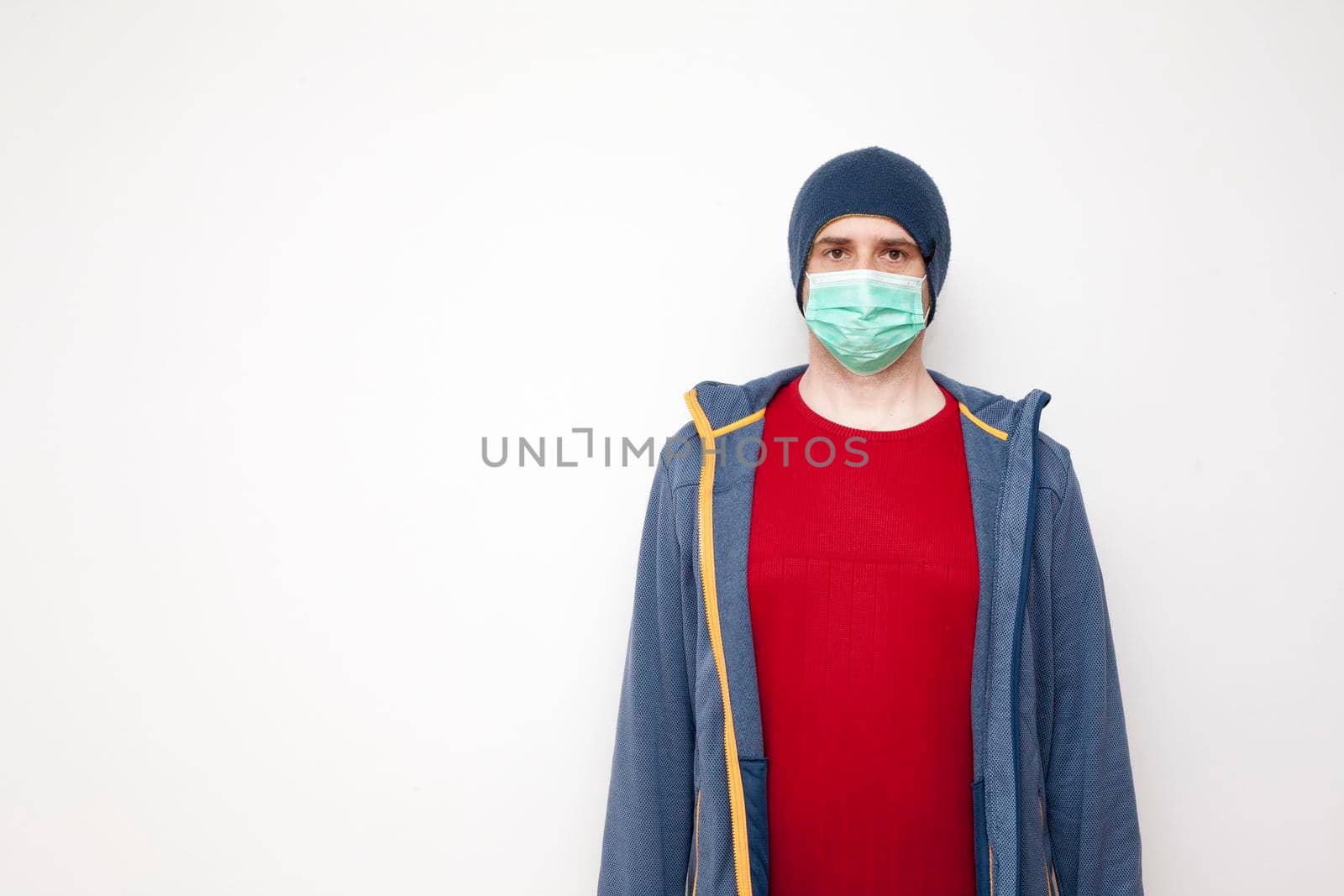 Man with green protective mask on white background. A man with a red sweater and a blue jacket, with a hood.