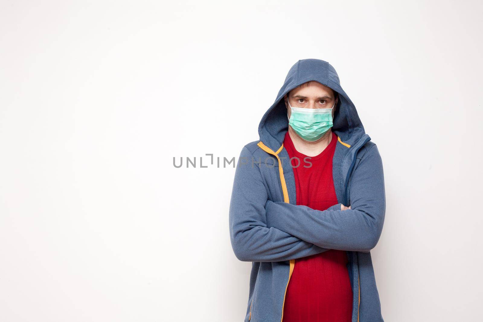 Man with green protective mask on white background. A man with a red sweater and a blue jacket, with a hood.