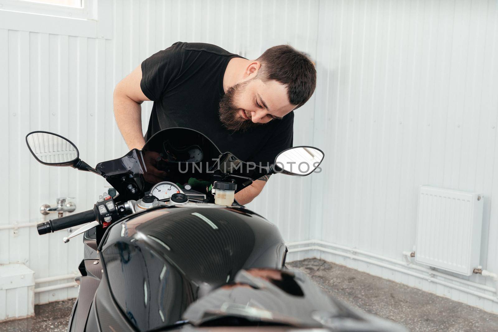 Young man cleaning or working with BMW black motorbike. Modern powerful motorcycle