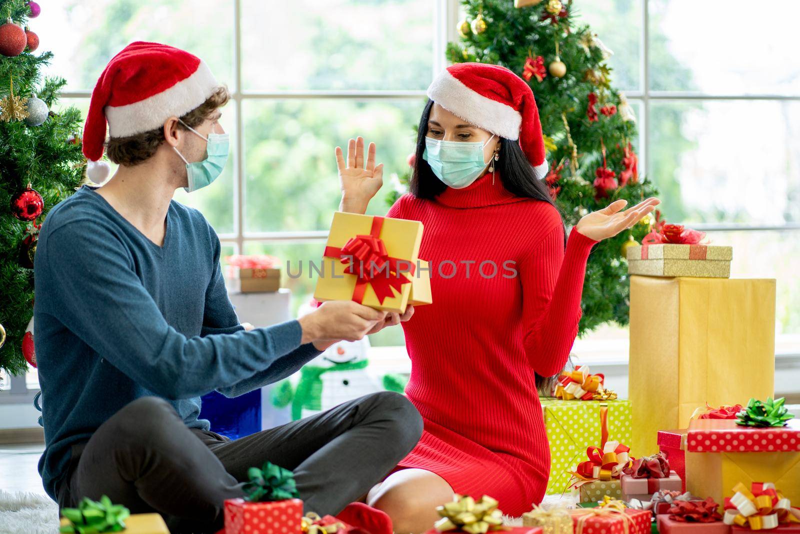 Caucasian man with hygiene mask show the present or gift to his couple woman and she action of surprise for Christmas celebration during pandemic of Covid-19.