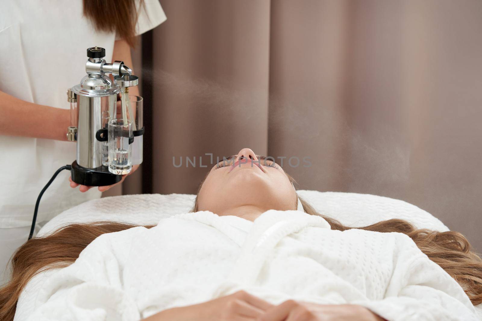 The procedure of steaming the skin of the face of a young woman before cleaning the skin in spa salon