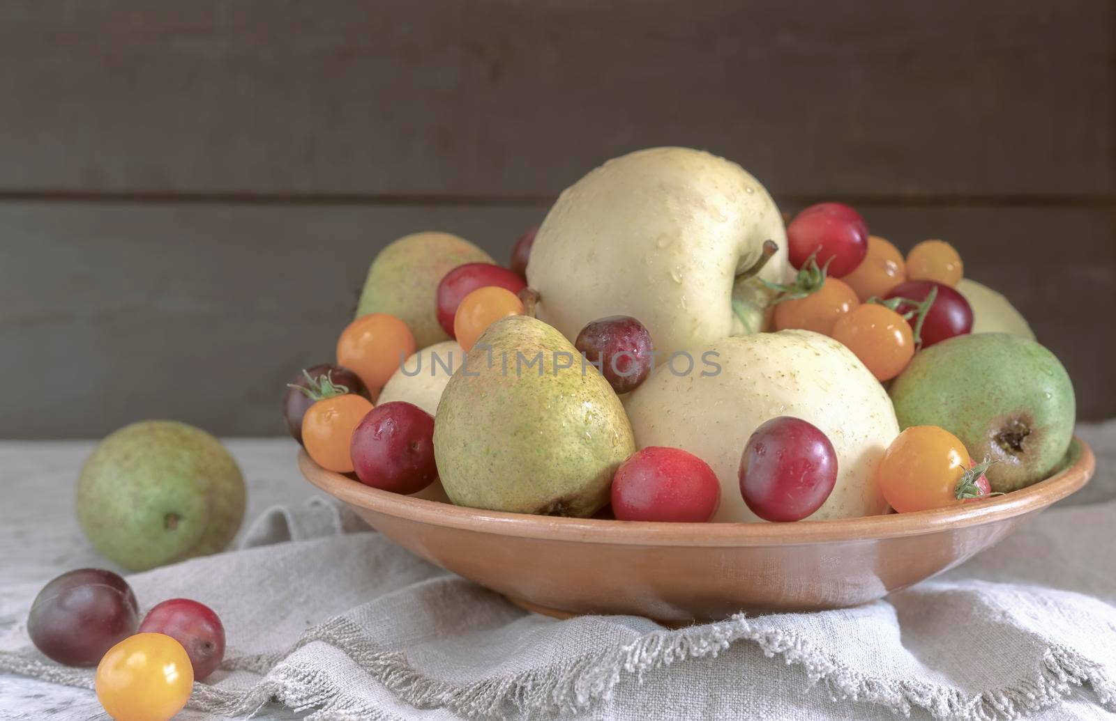 Still life: apples, pears, plums in a ceramic plate. Presented in close-up on a dark background. Front view, copy space
