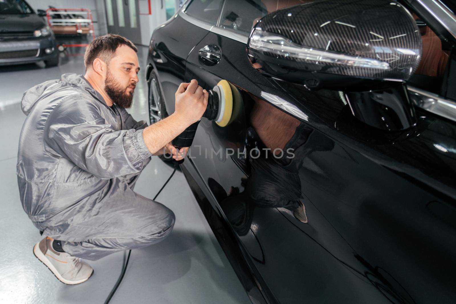 Worker polishing vehicle body with special grinder and wax from scratches at the car service station