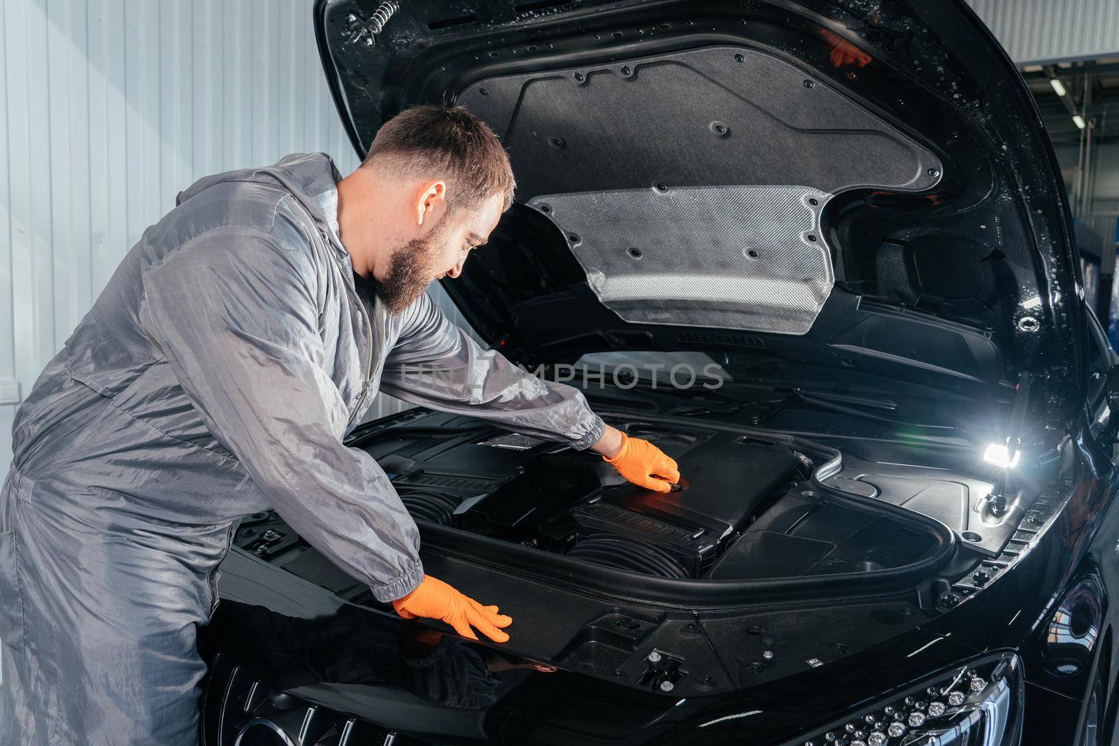 Car mechanic with open car hood for internal checking to maintenance vehicle by customer claim order in auto repair shop garage. Engine repair service