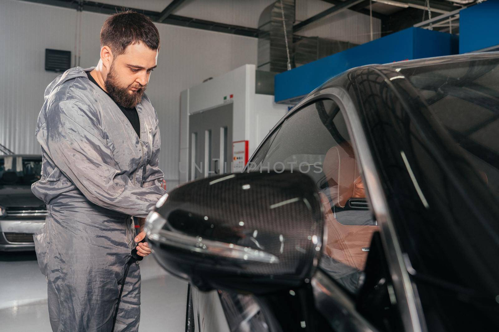 Worker polishing vehicle body with special grinder and wax from scratches at the car service station