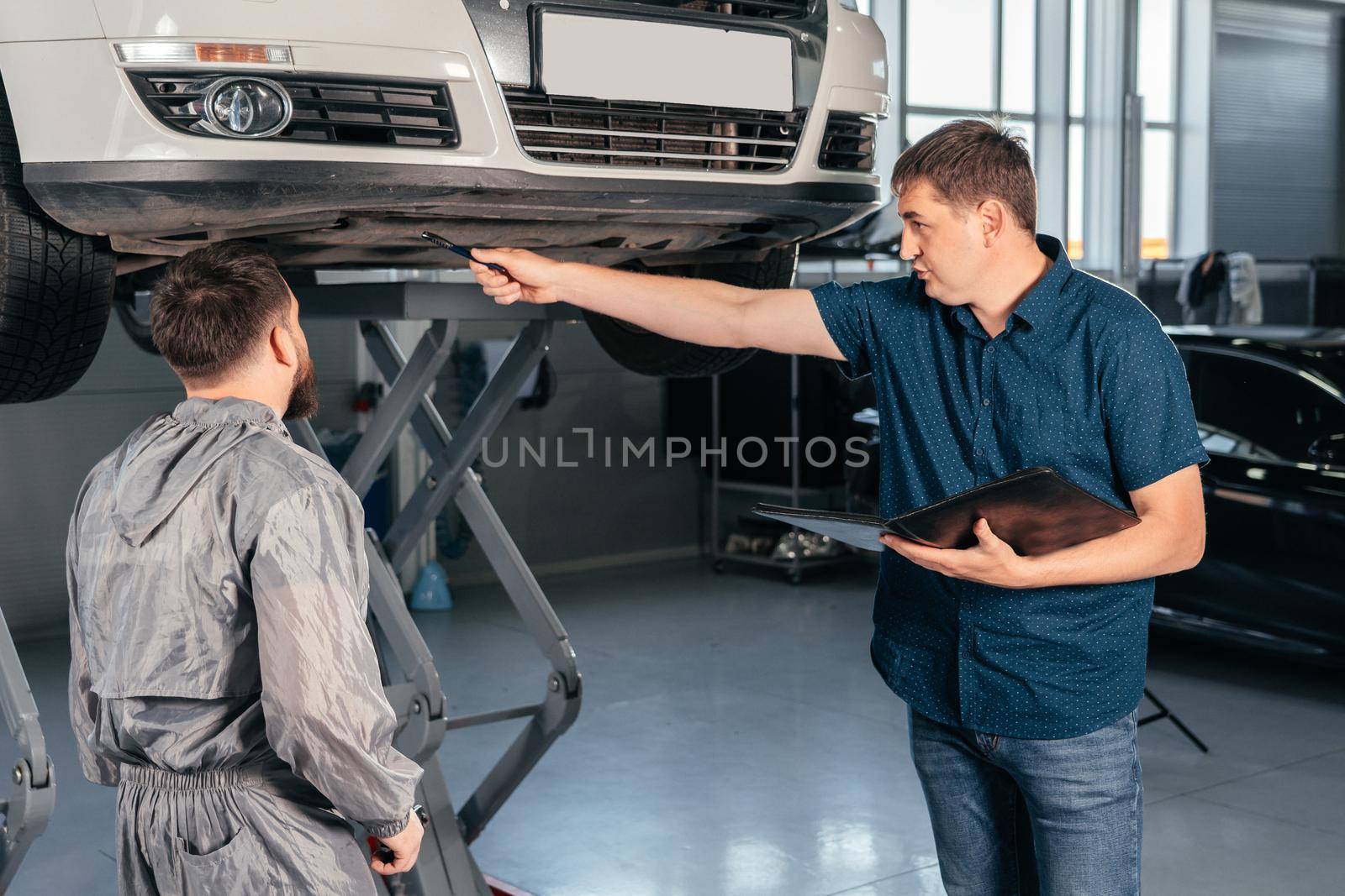 Mechanic Talking to a Manager Under a Vehicle in a Car Service. Boss showing what to fix