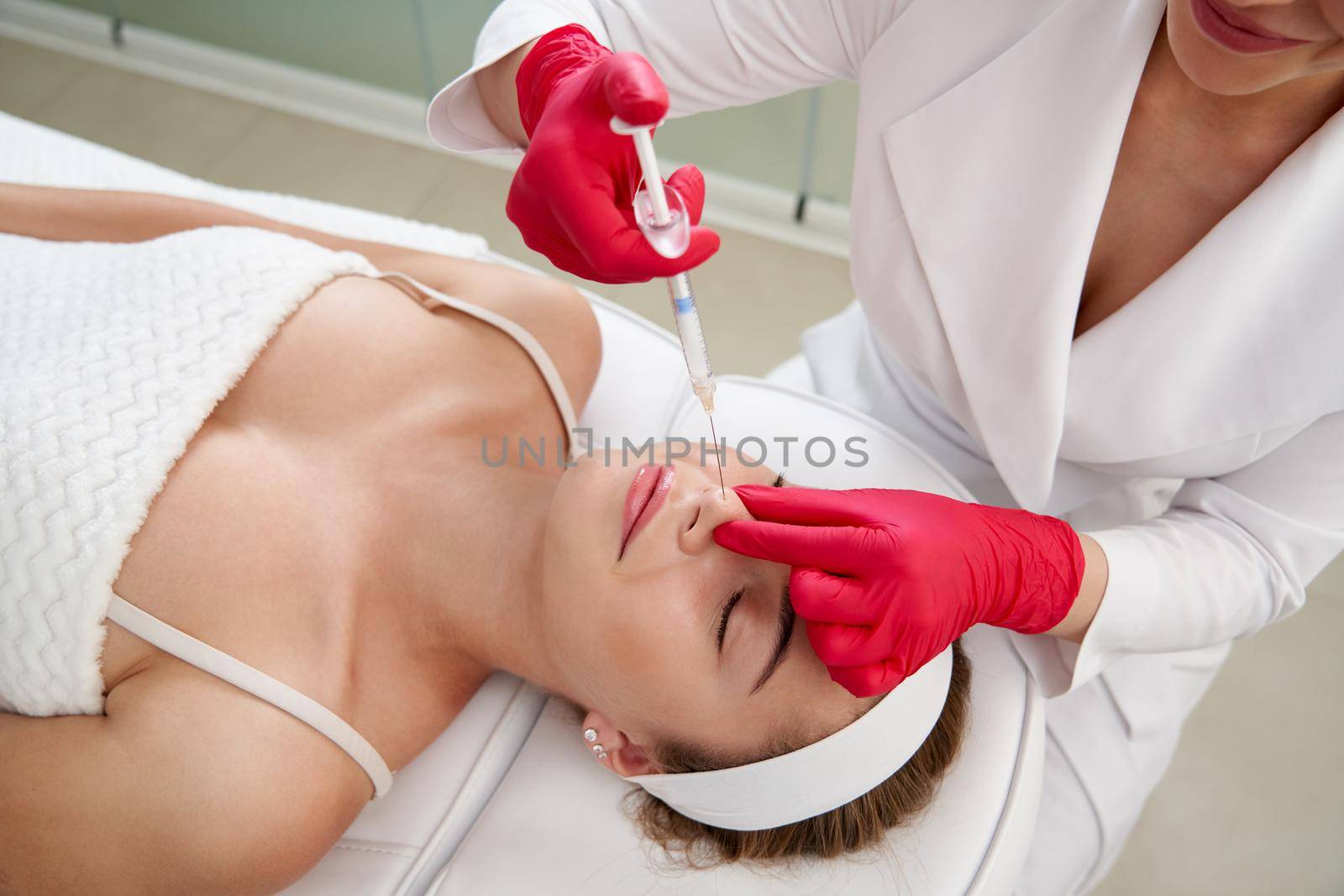 Beautician making injection in the nose with syringe in beauty salon. Cosmetic rejuvenating facial treatment
