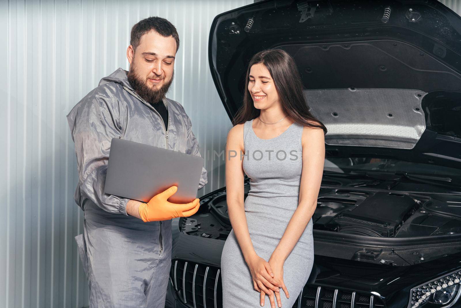 Car mechanic communicating with a customer while using laptop and examining vehicle breakdown at auto repair shop