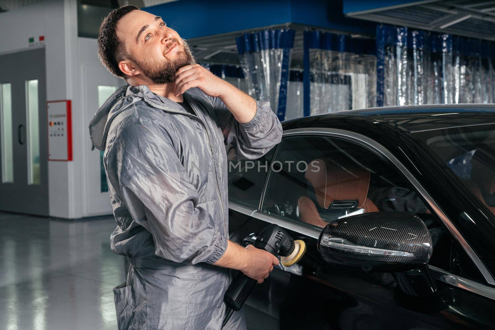 Worker polishing vehicle body with special grinder and wax from scratches at the car service station