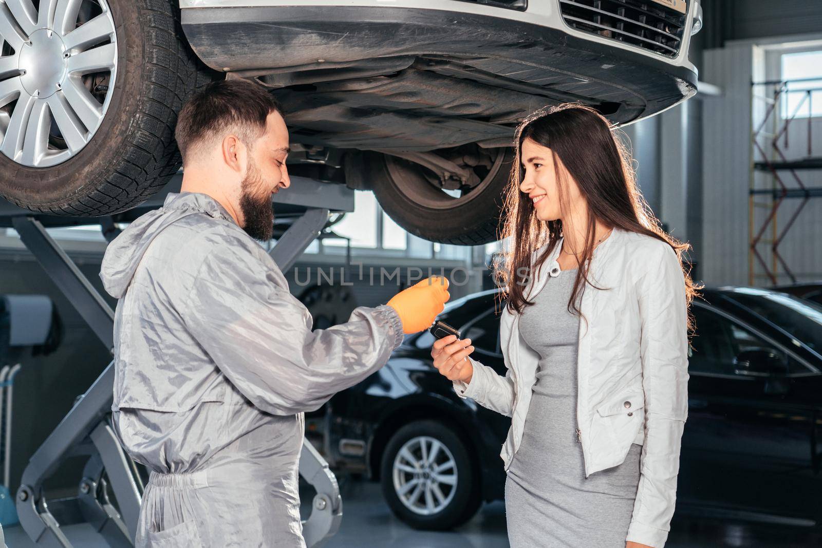 Auto Mechanic giving the car keys to his female customer in workshop at auto repair center. Quality of Service by Mariakray