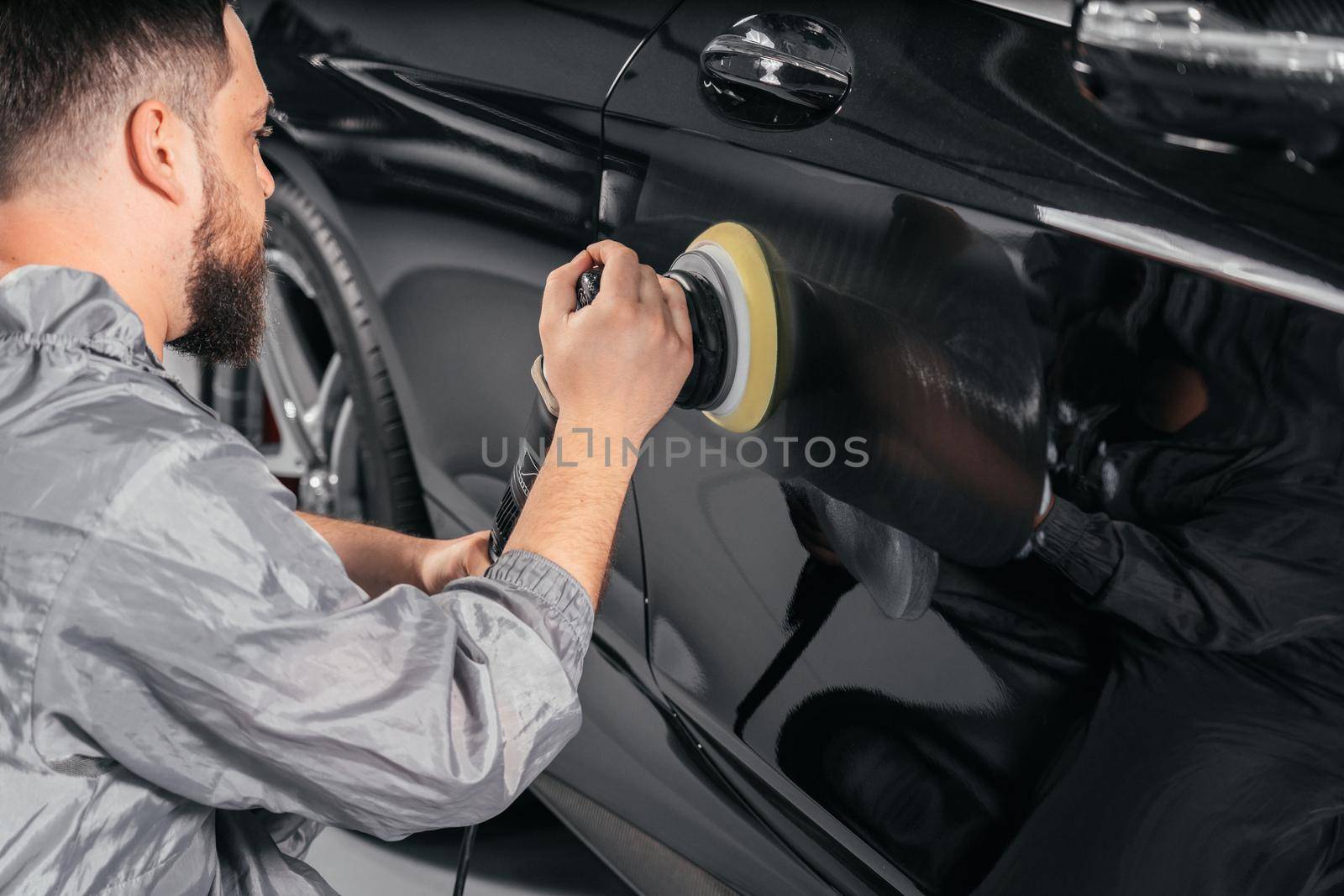 Worker polishing vehicle body with special grinder and wax from scratches at the car service station