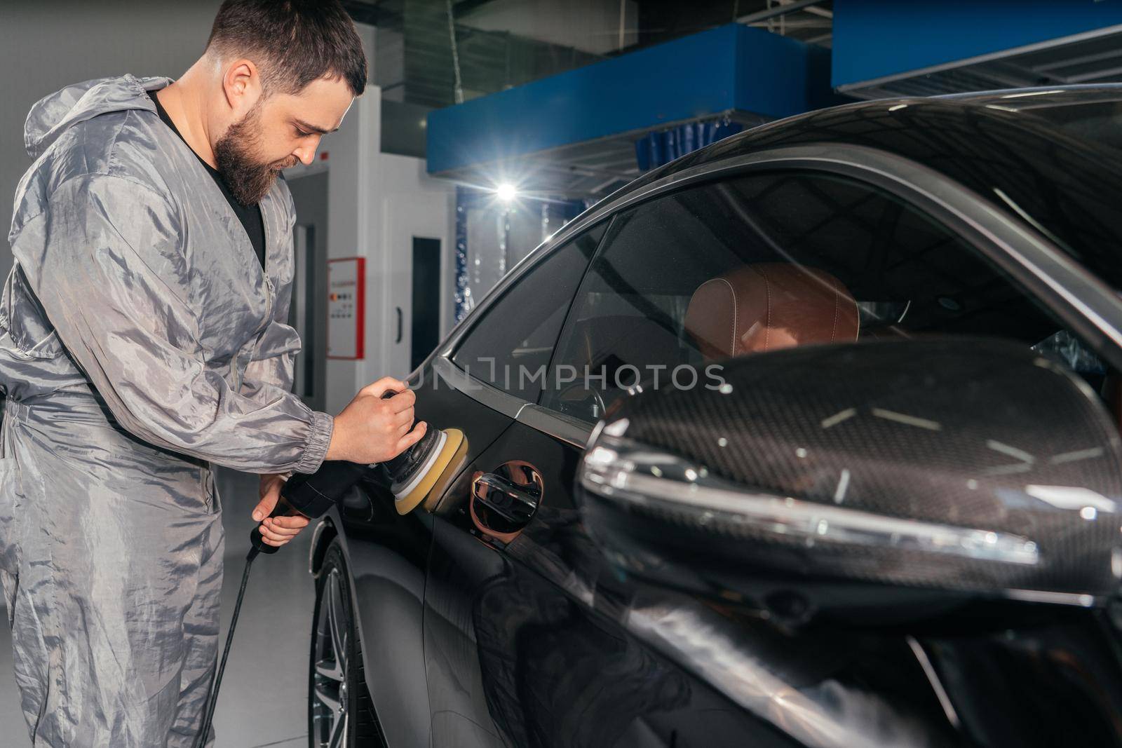 Worker polishing vehicle body with special grinder and wax from scratches at the car service station