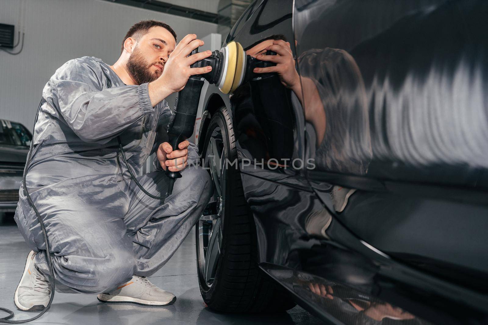 Worker polishing vehicle body with special grinder and wax from scratches at the car service station