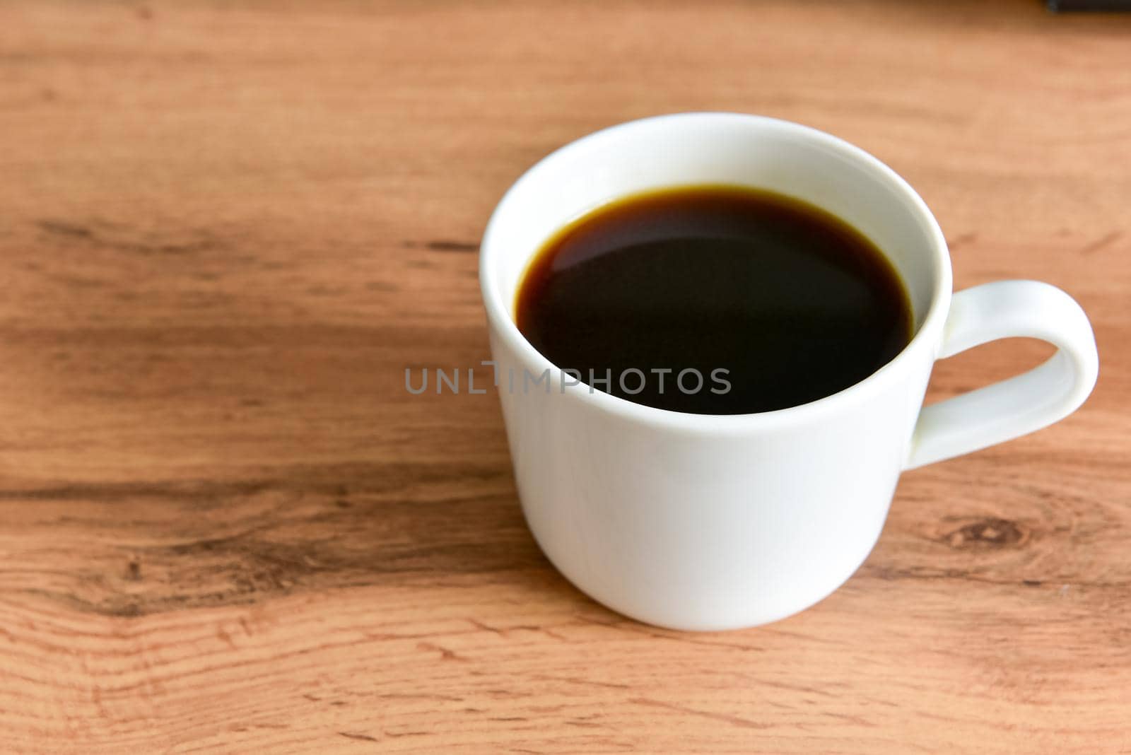 White cup of strong black coffee on wooden surface close up.