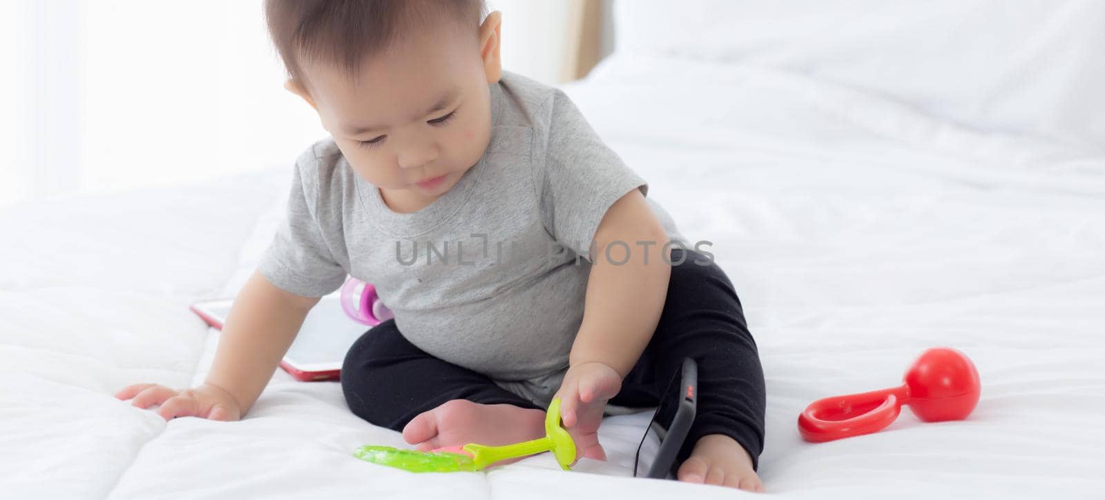 Portrait of cute little baby girl sitting with cozy on bed at bedroom, happiness of toddler, newborn 6-11 months with innocence and expression with cheerful, child charm, indoors, one person.