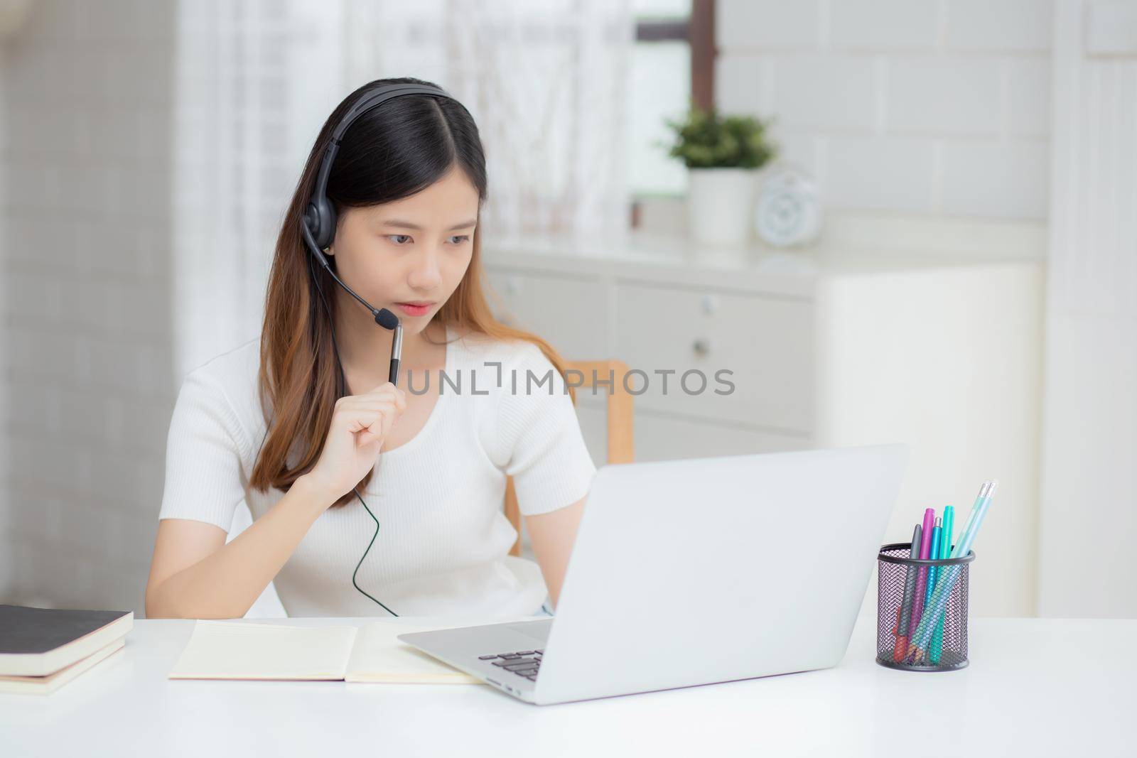 Young asian woman wearing headphone study online with e-learning on desk, girl wearing headset learning to internet with laptop computer at home, new normal, distance education and training. by nnudoo