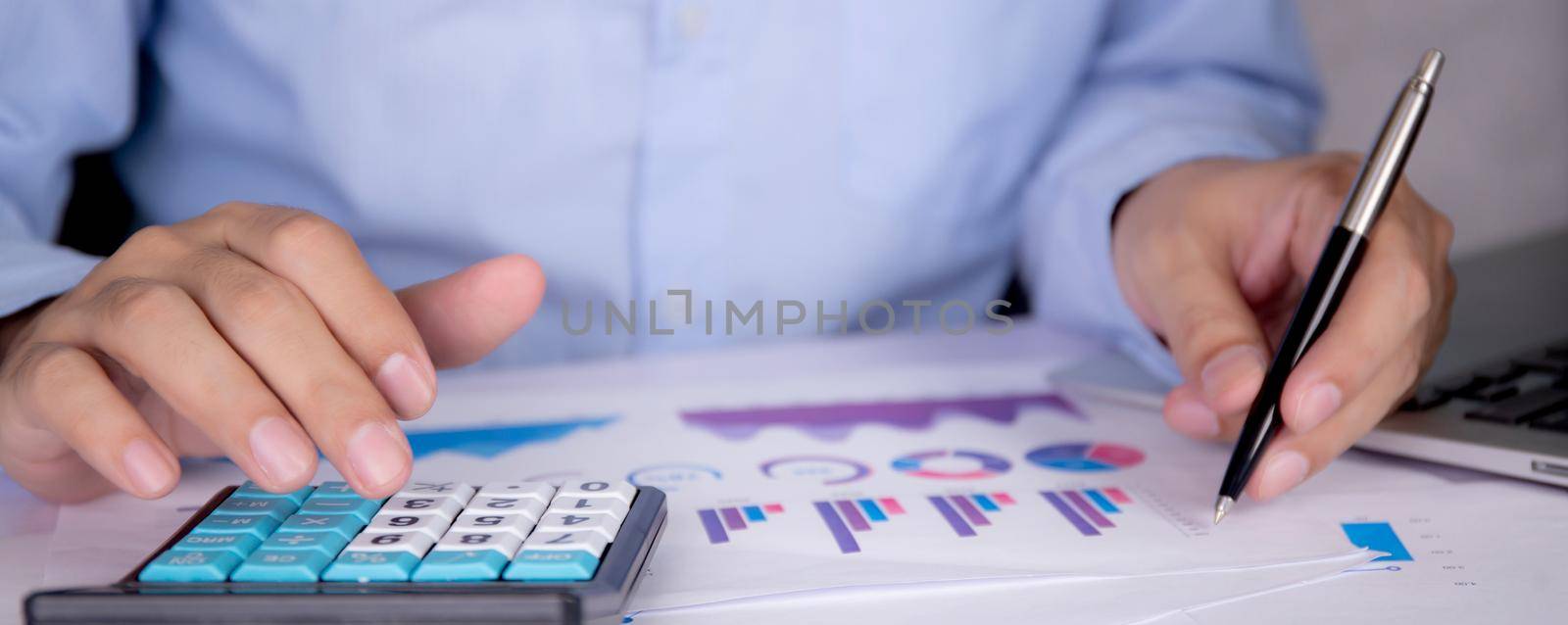 Hands of businessman calculate tax with calculator while laptop computer on desk, man planning finance and investment with graph and chart, statistic and examining account, business concept. by nnudoo