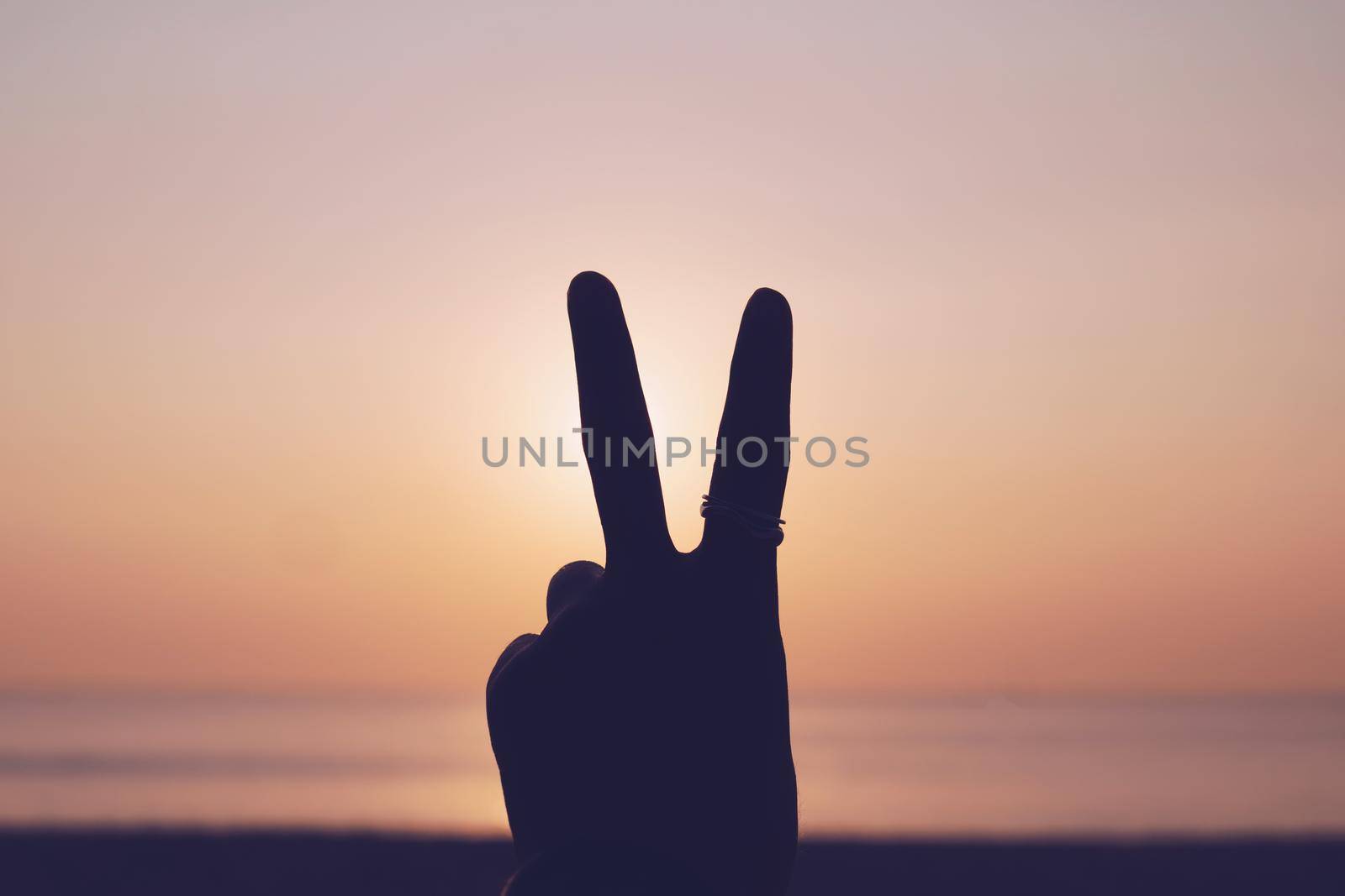 Peace out or fighting metaphor two fingers hand sign in front of a sunset. by Suwant