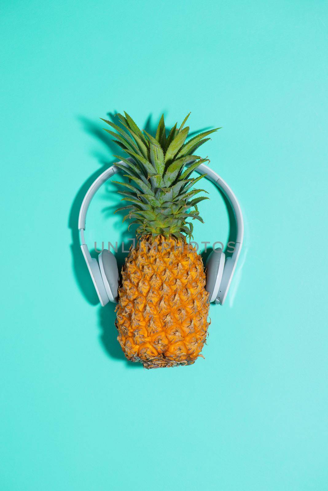 Fashion pineapple with headphones listens to music over blue background
