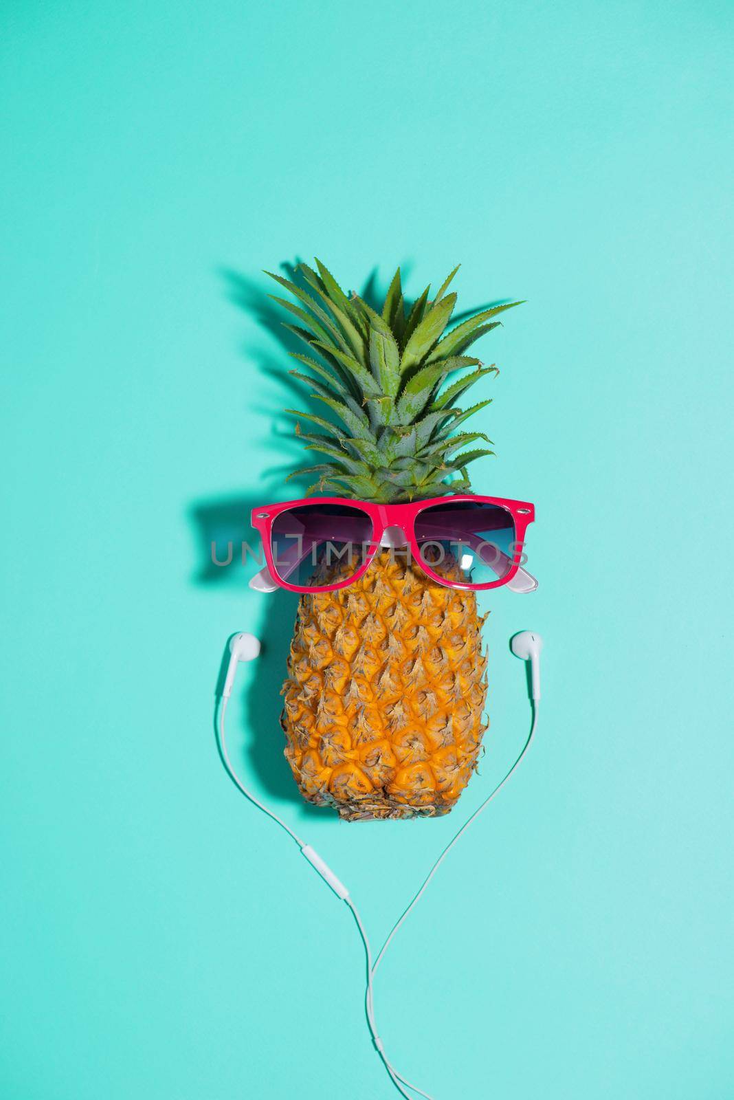 Fashion pineapple with sunglasses and headphones listens to music over blue background