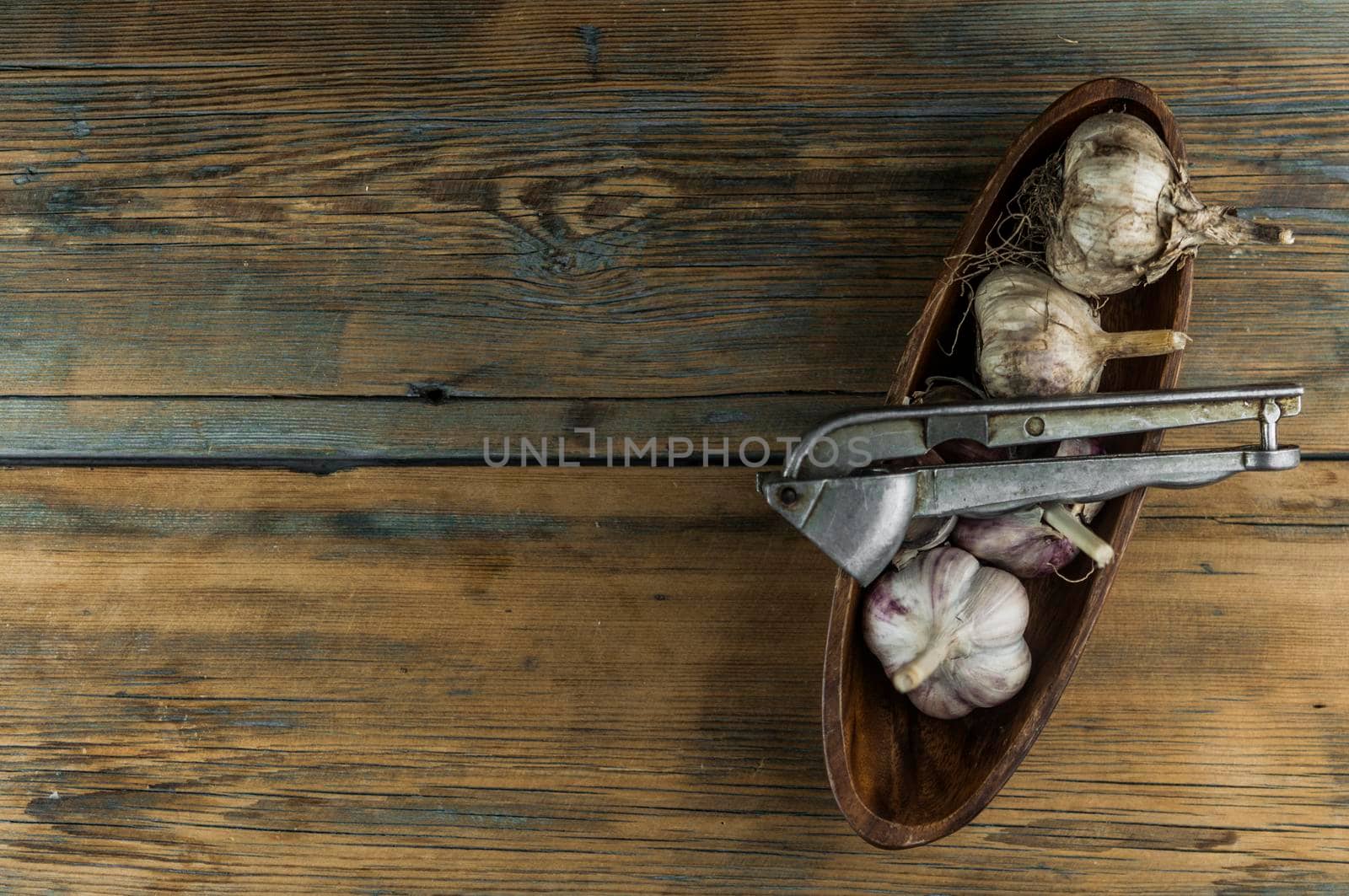 Organic garlic with metal press. Fresh garlic cloves and garlic bulb on a wooden table. Garlic for healthy eating. Concept of spices for healthy cooking. Closeup by inxti