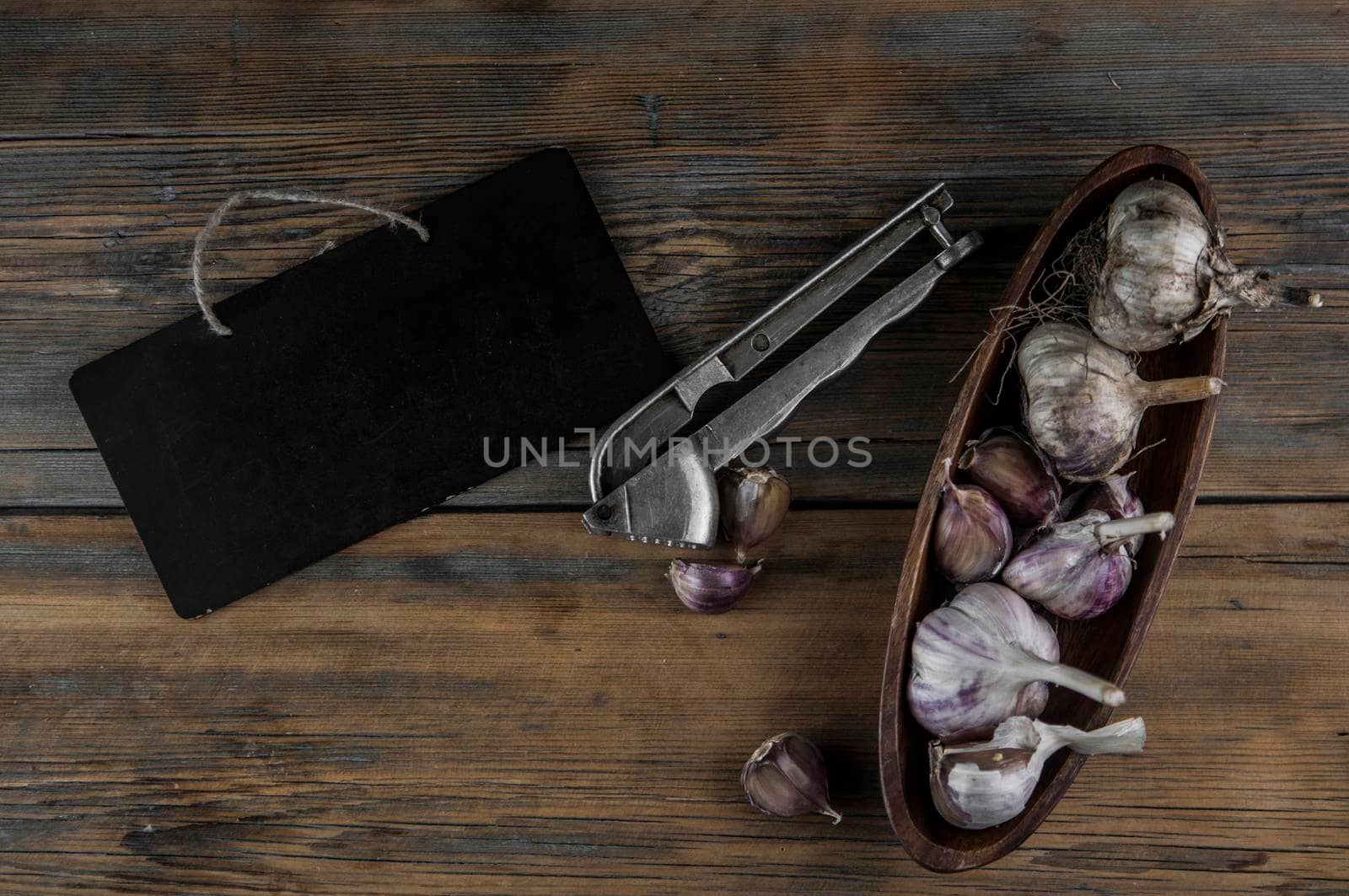 Organic garlic with metal press. Fresh garlic cloves and garlic bulb on a wooden table. Garlic for healthy eating. Concept of spices for healthy cooking. Closeup by inxti