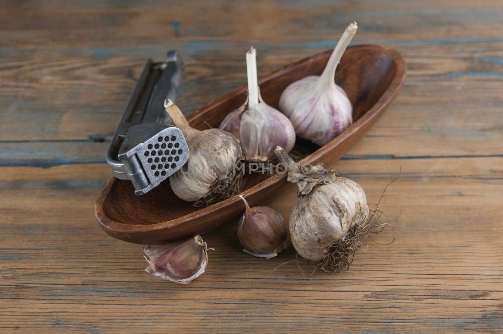 Organic garlic with metal press. Fresh garlic cloves and garlic bulb on a wooden table. Garlic for healthy eating. Concept of spices for healthy cooking. Top view