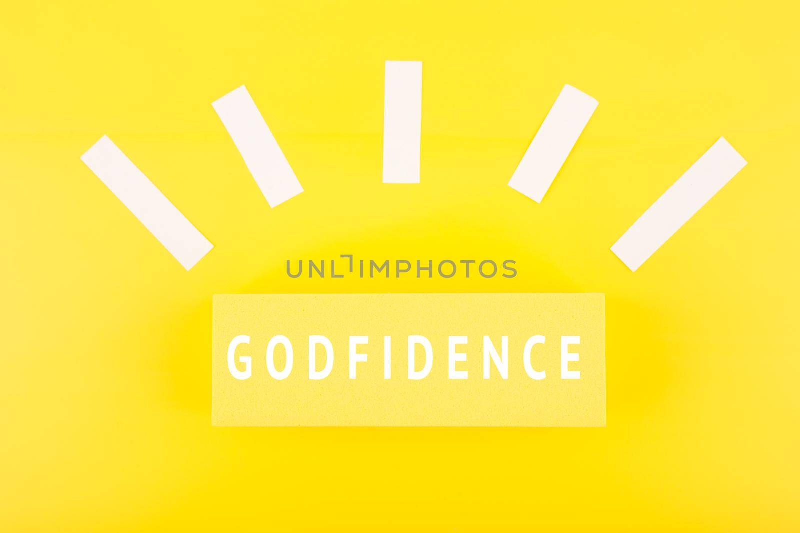 Godfidence single word against bright yellow background with rays of light made of paper. Modern biblical creative religious concept 