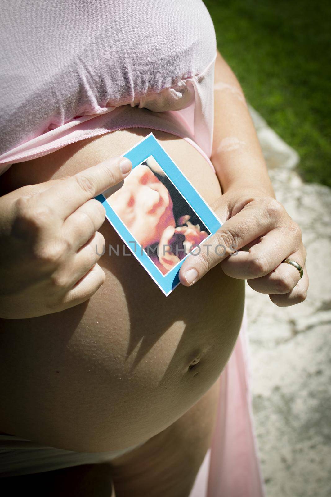 Seven month pregnant woman with ultrasound of baby on her gut. Pink dress color