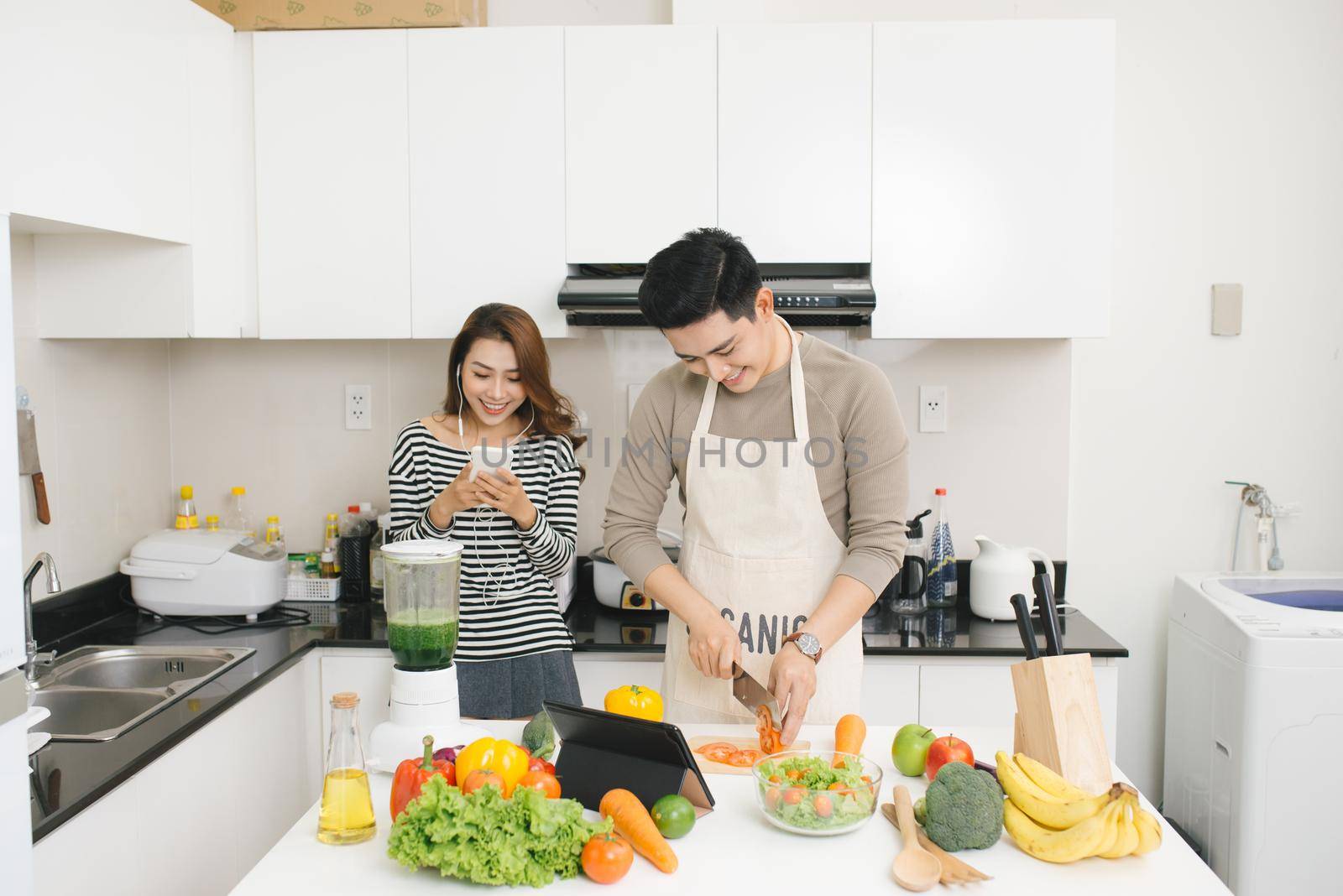 Asian woman using cell phone while a man prepares a meal by makidotvn