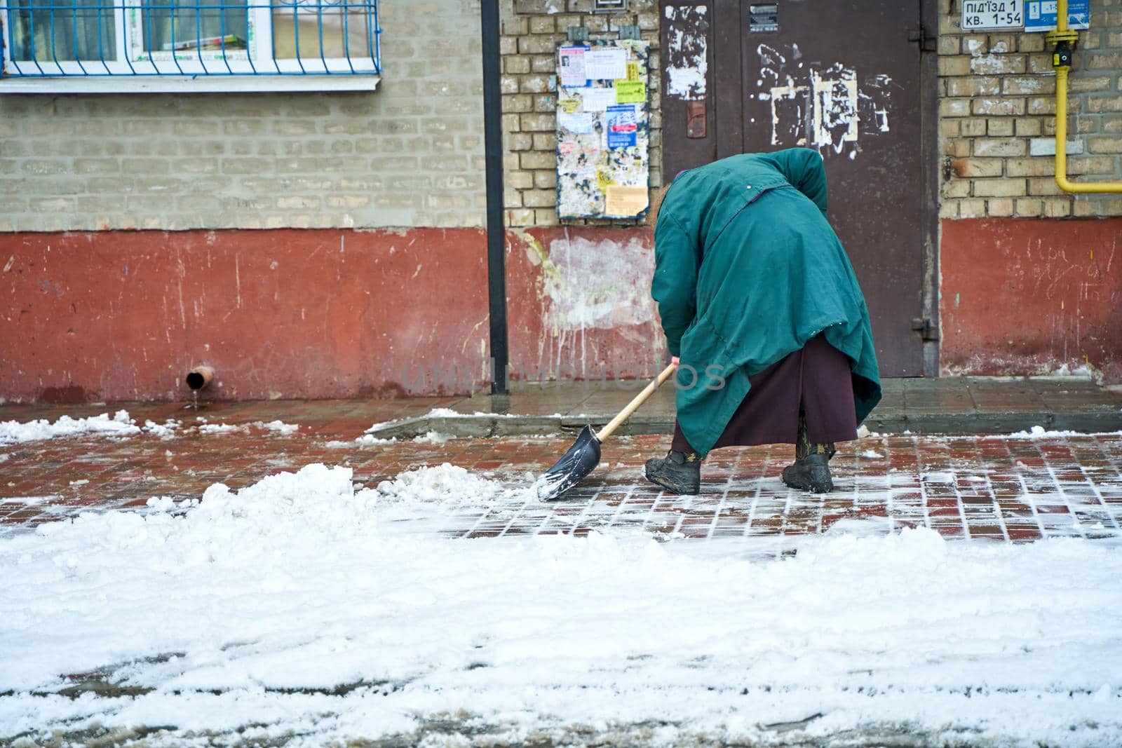 An old grandma yard man clears the snow on entrance.