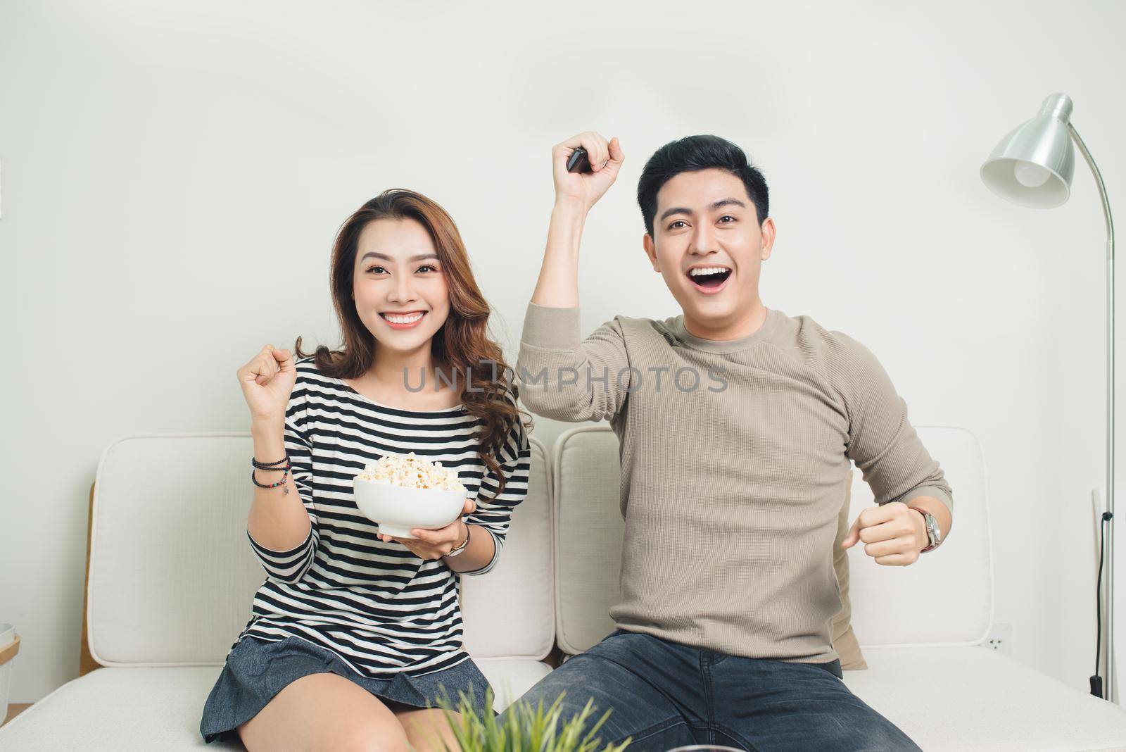 Excited young asian couple watching TV and eating popcorn