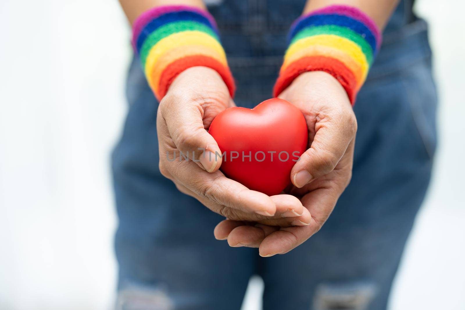 Asian lady wearing rainbow flag wristbands and hold red heart, symbol of LGBT pride month celebrate annual in June social of gay, lesbian, bisexual, transgender, human rights.