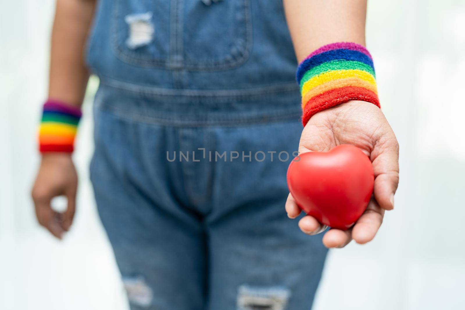 Asian lady wearing rainbow flag wristbands and hold red heart, symbol of LGBT pride month celebrate annual in June social of gay, lesbian, bisexual, transgender, human rights. by pamai