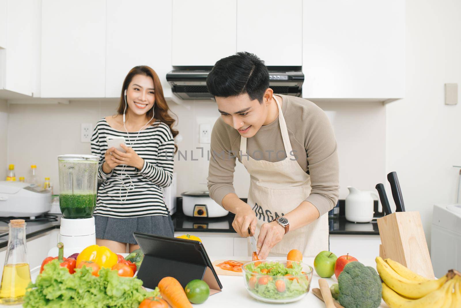 Asian woman with phone while a man prepares a meal by makidotvn