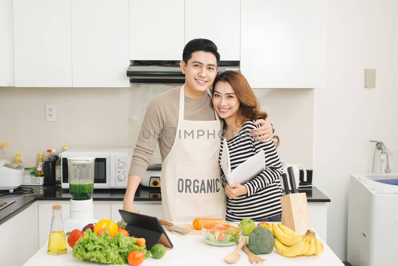 Happy asian couple following recipe on digital tablet when cooking by makidotvn