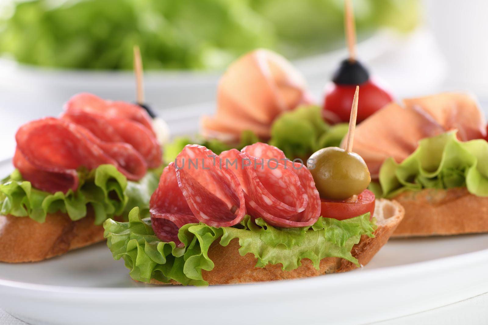 Tender baguette canapes with Leaf lettuce, salami or Parma ham, tomatoes, mozzarella and olive. Delicacy assorted platter for at the party.