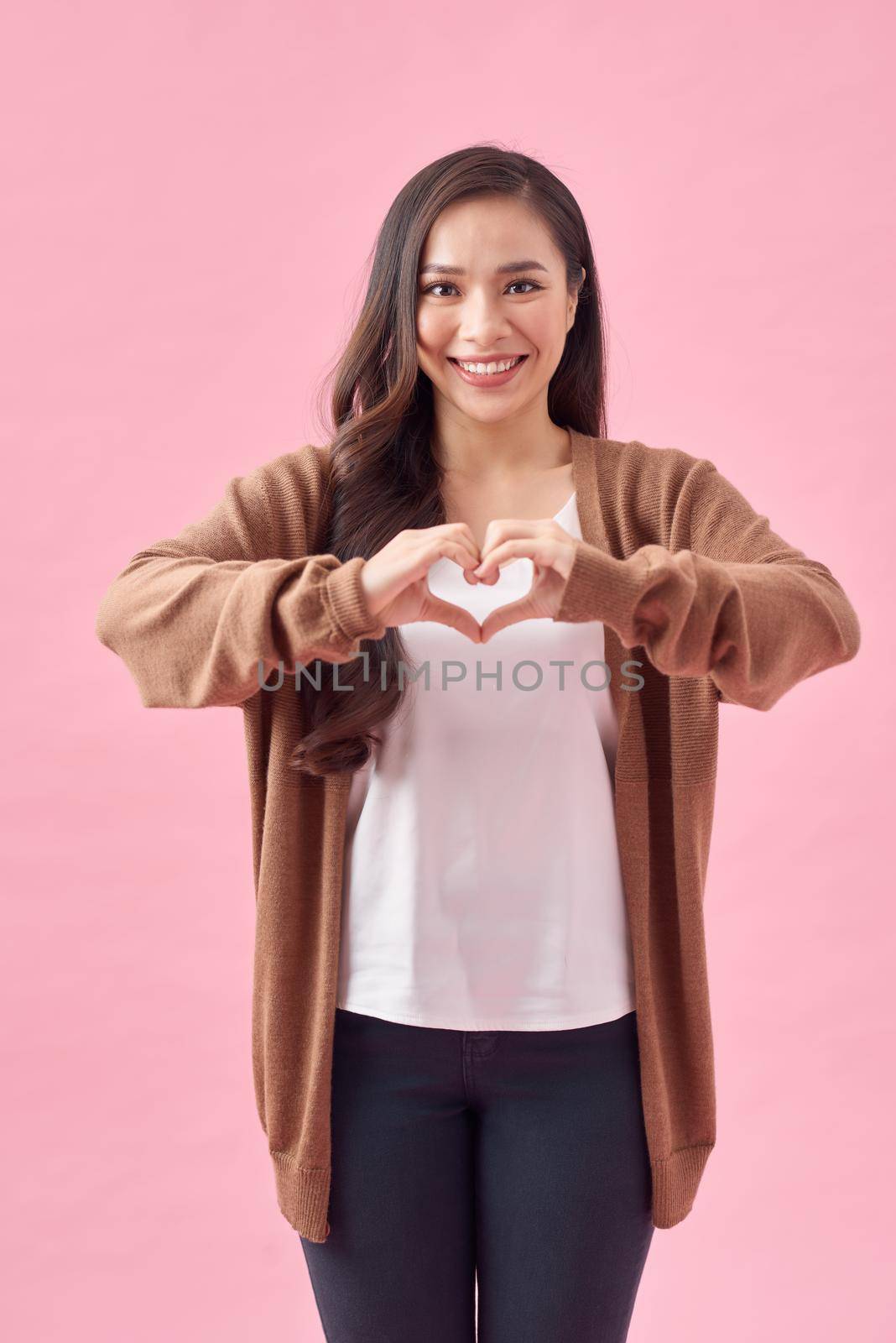 Asian woman making a heart shape with her hands, isolated over pink background