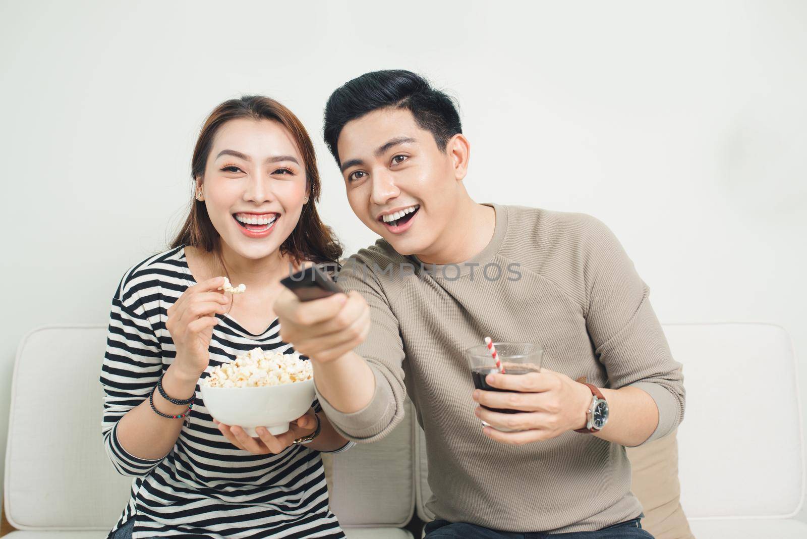 Excited young asian couple watching TV and eating popcorn