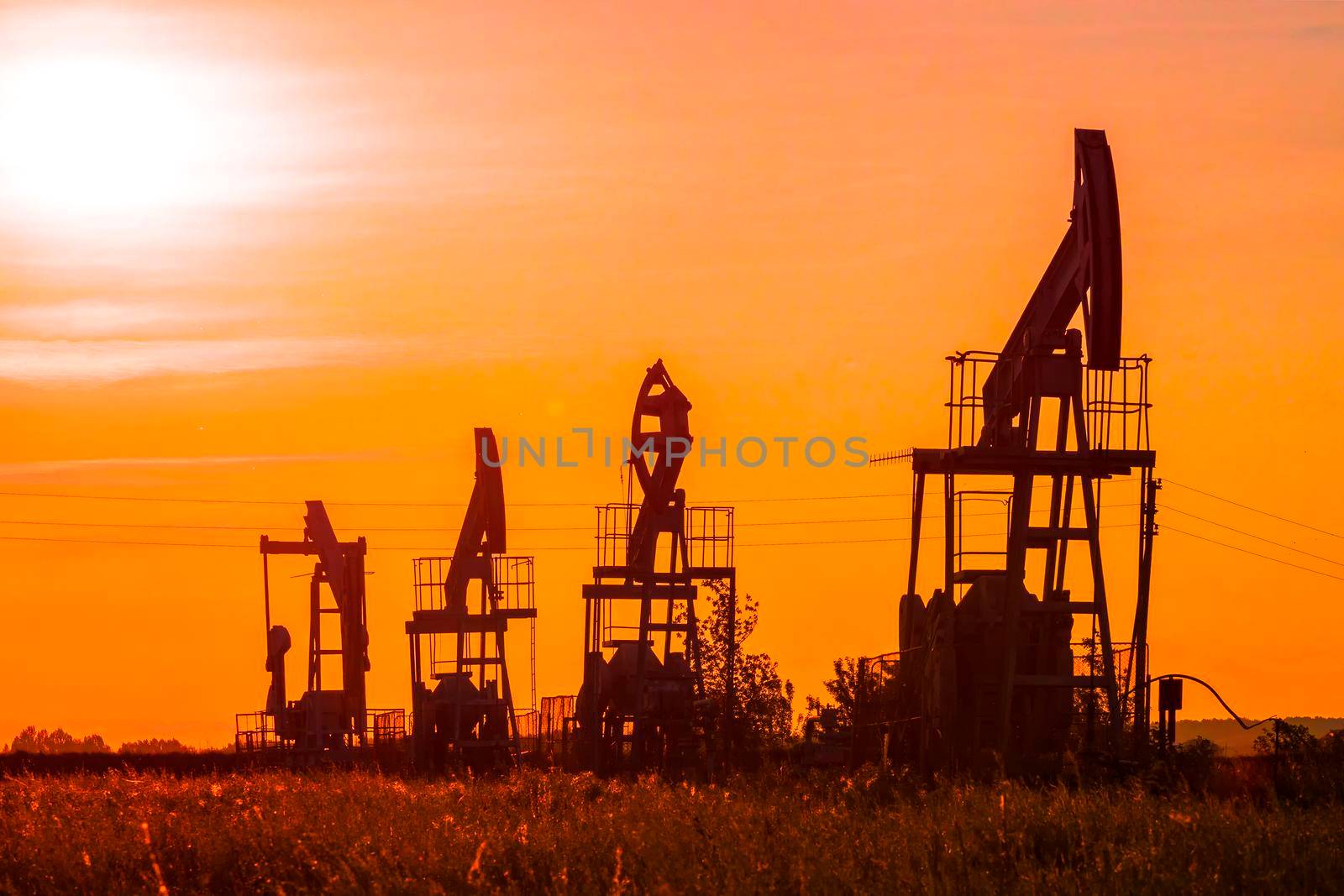 The silhouette of oil pumps in a large oil field at sunrise. by Essffes