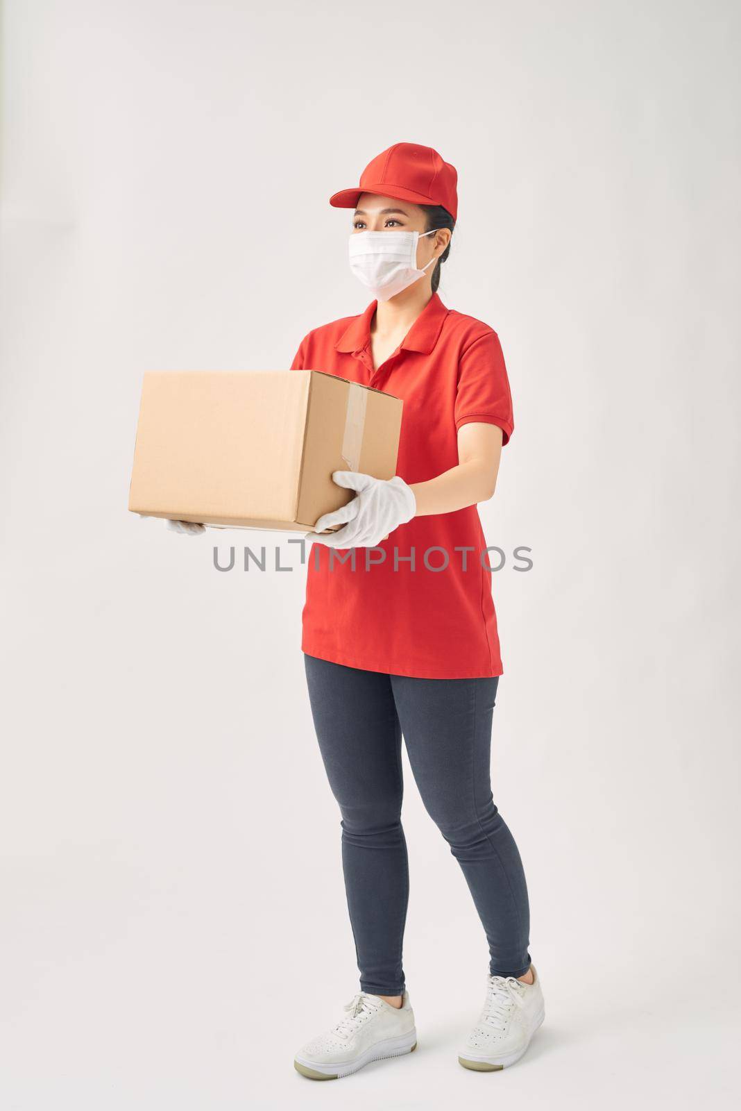 A uniformed courier wearing medical rubber gloves and a medical mask holds a paper box of food on a white background.  by makidotvn