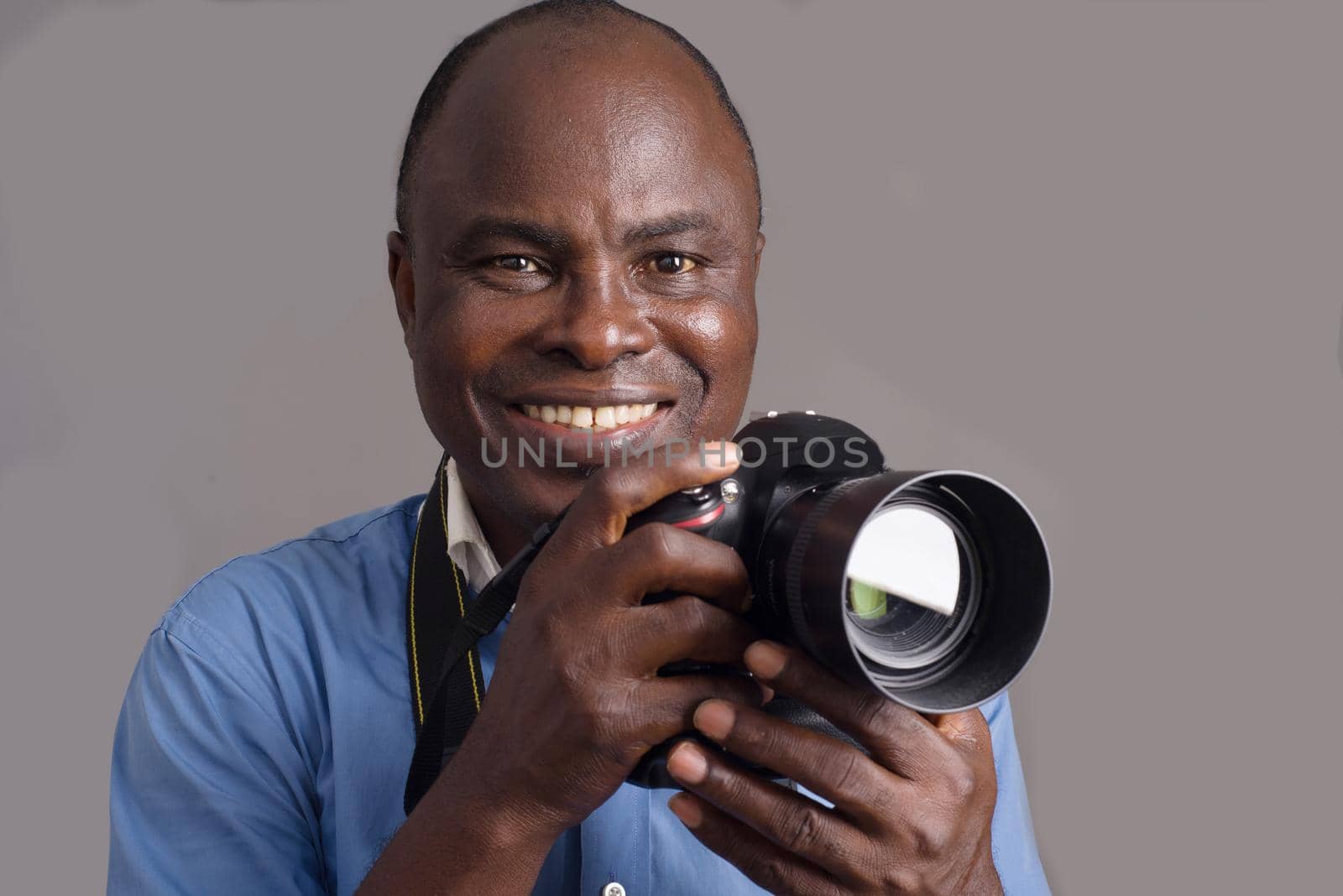 African man standing in blue shirt on gray background looking in front of him and finger on camera shutter smiling.