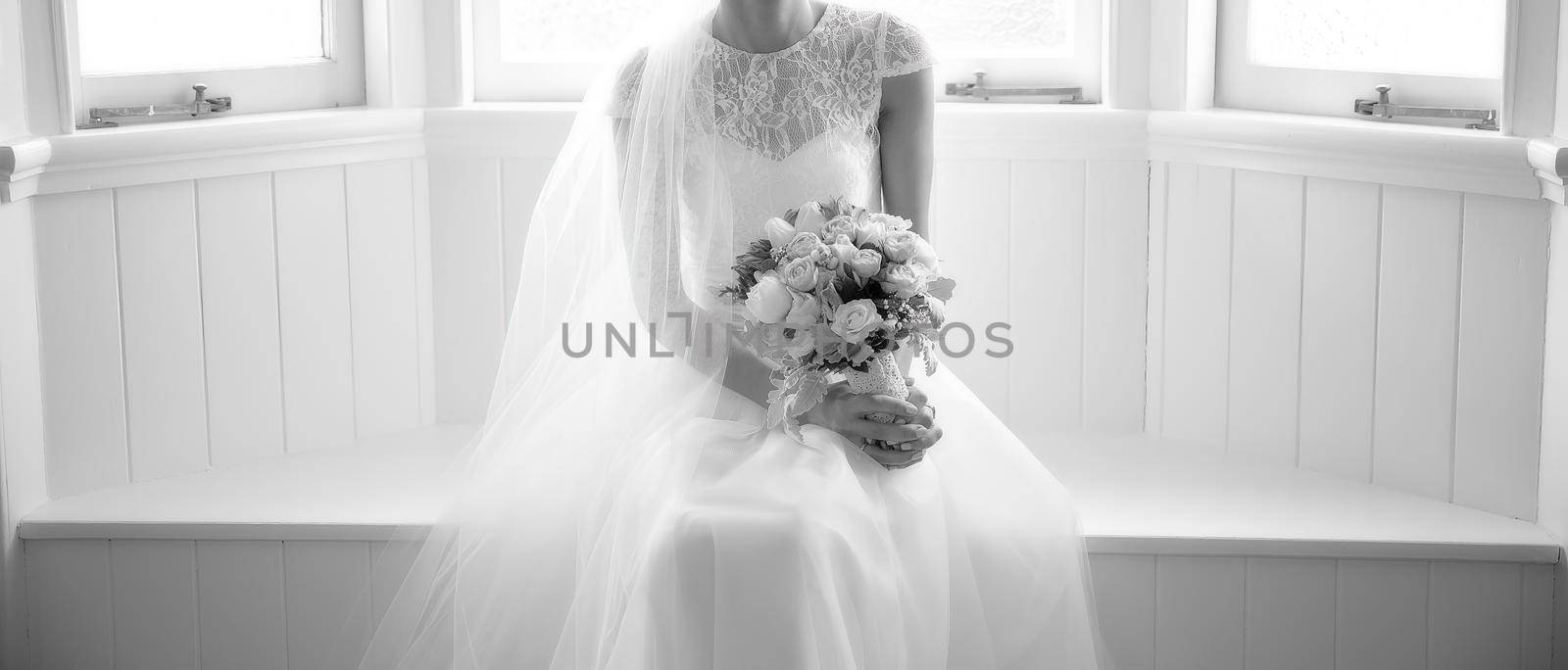 A bride holding her bouquet in dreamy soft window light as she poses before her wedding - monotone image
