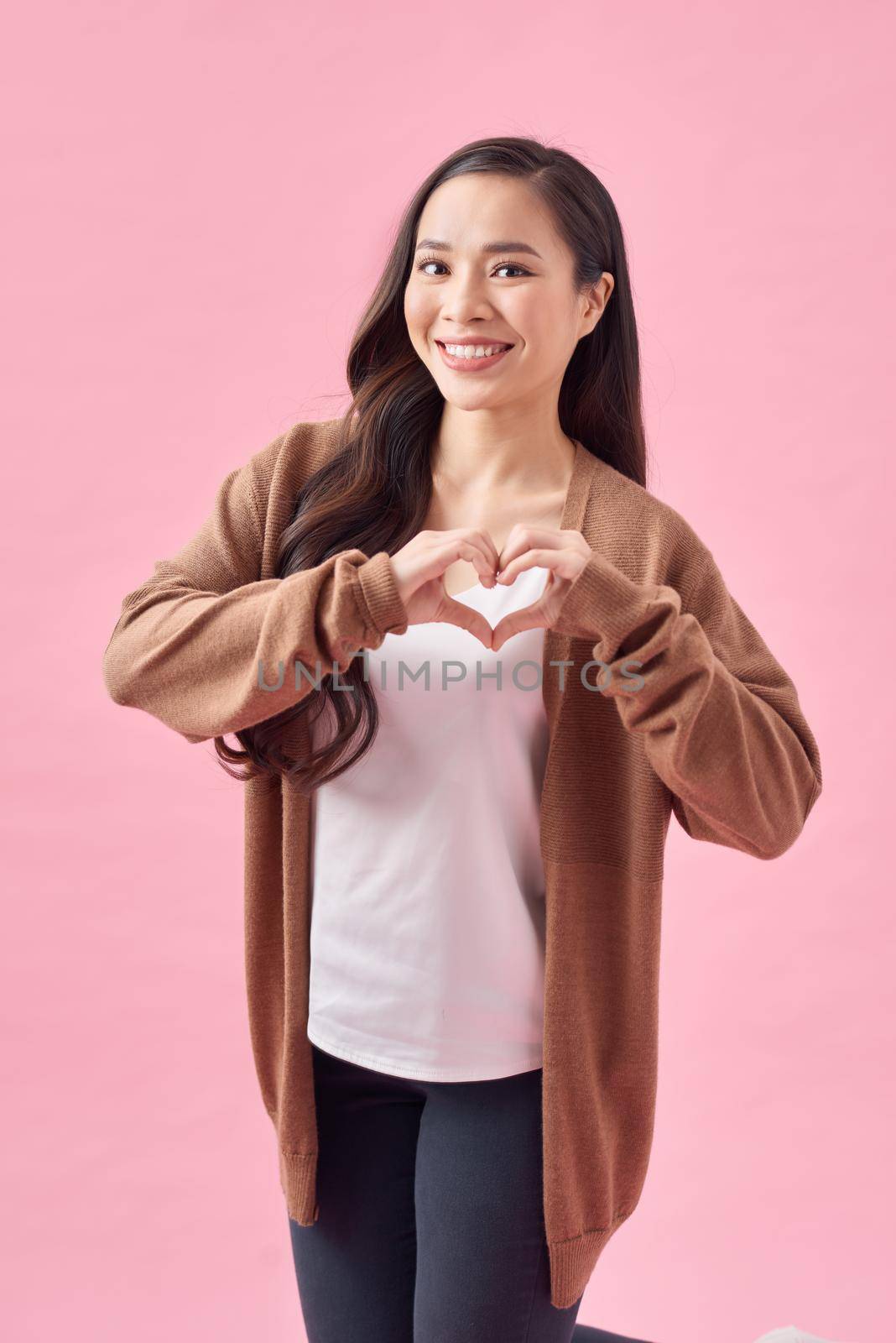 Happy woman make heart shape by her hands, closeup portrait on pink background.