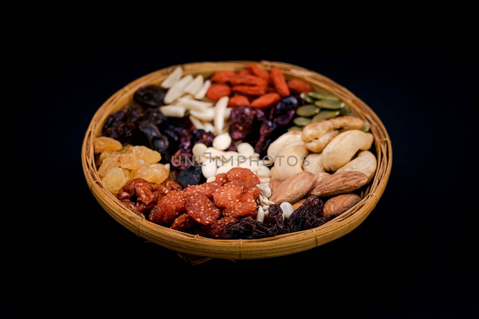 Group of various types of dried fruits and dried on a bamboo tray on black background.